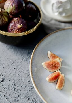 High angle view of fresh purple fig wedges on a ceramic plate next to a bowl of whole figs.