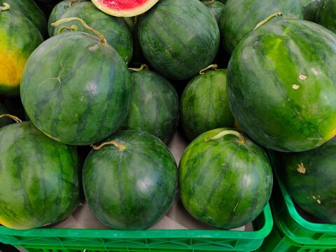 Round green-striped red watermelons with intact dried stems piled together in a fresh produce display.
