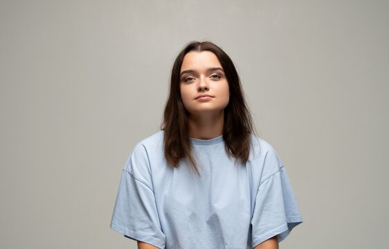 Young woman portrait in studio, brown hair and blue tee, calm confident gaze, minimal neutral background with copy space