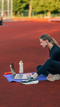 Woman using laptop for online fitness class outdoors on a sunny day