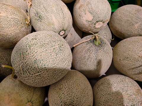 A close-up view of fresh whole red sweet melons, featuring their distinct webbed rind textures piled together in a market display.