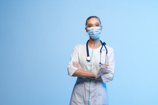Medical worker wearing personal protective equipment, looking at camera and holding syringe on blue background