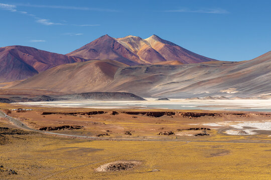 View of the red volcanic rock formations and salt flats of Piedras Rojas set against a backdrop of arid mountains under a clear blue sky in Chile.