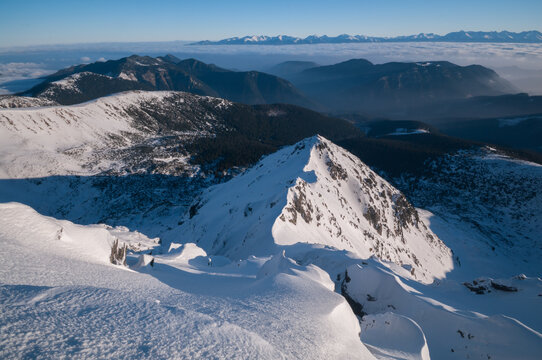 View of the snow-covered peak of Dumbier in the Low Tatras, featuring dramatic mountain ridges, deep shadows, and a vast winter landscape in Nizke Tatry, Zilina Region, Slovakia.