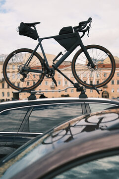 Touring bicycle equipped with travel bags carried on a car roof in an urban setting, representing cycling tourism, active vacations and travel with a bike.