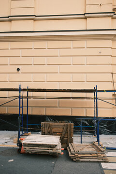 Scaffolding and stacked wooden platforms beside a classical urban facade during maintenance work, illustrating property renovation and preservation of existing buildings.
