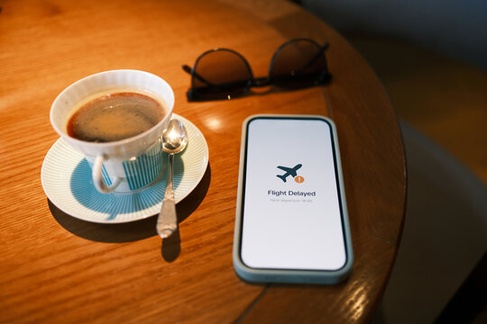 Smartphone displaying a flight delay notification beside coffee and eyeglasses on a table, illustrating travel disruption, changing plans and passenger inconvenience.