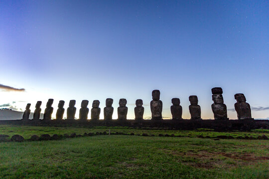 View of the iconic Moai statues at Ahu Tongariki standing in a row against a twilight sky on Easter Island, Valparaiso, Chile.