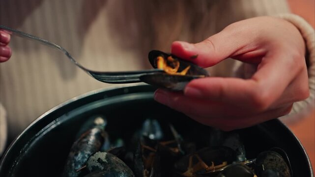 Woman hands holding mussel shell and removing cooked mussel meat with fork seafood closeup.