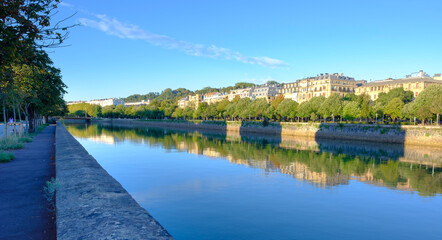 Fototapeta premium Riverside promenade with city buildings reflecting in water along Urumea river, Donostia San Sebastian, Basque Country, Spain
