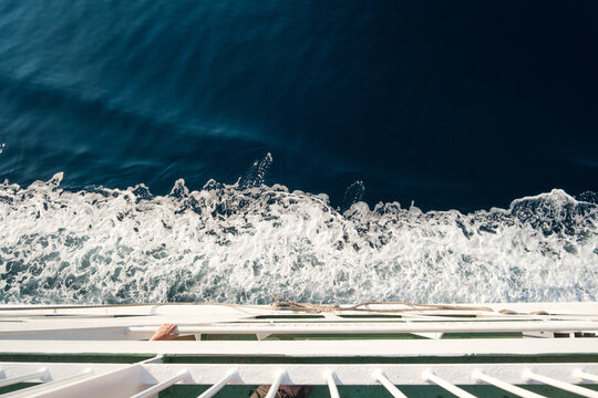 View of the churning white wake of a ferry boat against the deep blue sea, captured from the deck railing at Misnjak Ferry Port in Barbat na Rabu, Primorsko-goranska zupanija, Croatia.