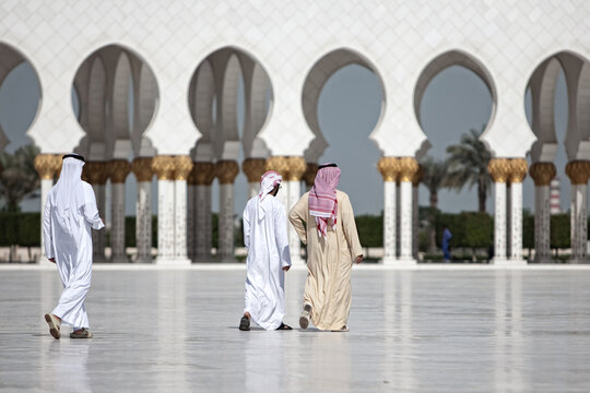 View of three men in traditional clothing walking in front of a white arched colonnade in the United Arab Emirates.