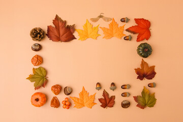 Fototapeta premium Autumn frame made of colorful maple leaves, acorns, pine cone and miniature pumpkins on a warm peach background, photographed from directly above. Seasonal composition with generous copy space.