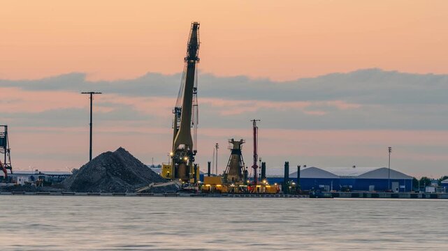 Helsinki, Finland - 22 July 2026: View of construction work at the West Harbour with a large crane vessel, gravel piles, and industrial buildings at sunset. Timelapse.