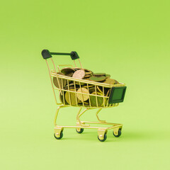 Miniature gold shopping cart overflowing with coins on a bright green background, photographed from a front three-quarter angle. Creative finance concept with clean negative space. © Bojan