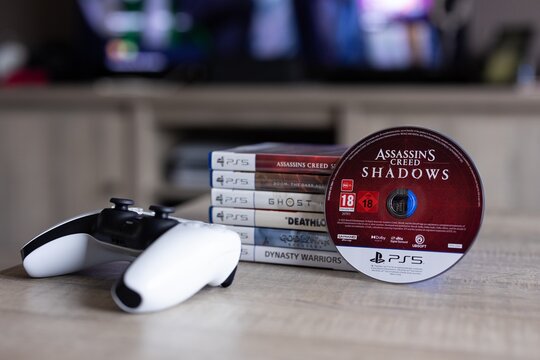 BRECHT, BELGIUM &ndash; August 28, 2026: Portrait of a stack of PS5 playstation games with a game disc standing against it and a controller lying next to it, highlighting physical gaming media.