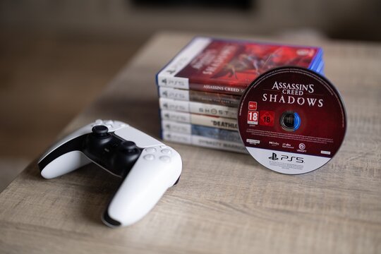 BRECHT, BELGIUM &ndash; August 28, 2026: Macro portrait of a stack of PS5 playstation games with a game disc standing against it and a controller lying next to it, highlighting physical gaming media.