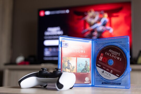 BRECHT, BELGIUM &ndash; August 28, 2026: Portrait of a PS5 game case standing open with a physical game disc in it and a playstation 5 controller lying next to it with the home screen in the background.