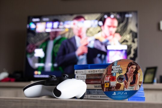 BRECHT, BELGIUM &ndash; August 28, 2026: Closeup portrait of a stack of PS5 games, a controller, a physical playstation game disc of GTA and a blurred home screen in the background.