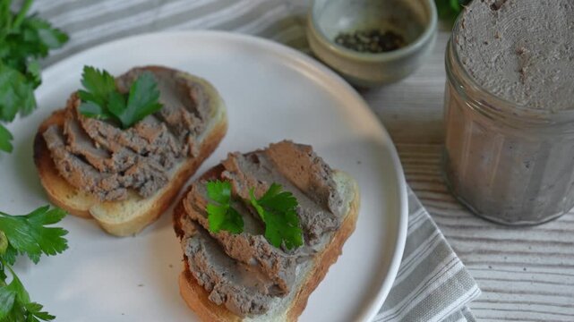 Homemade chicken liver pate in glass jar with toasted bread and herbs, top view. Liver pate for healthy eating.