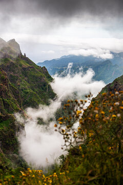 Dramatic mist and clouds swirling through lush volcanic valleys between Pico do Arieiro and Pico Ruivo in Madeira, showcasing wild nature and moody mountain scenery.