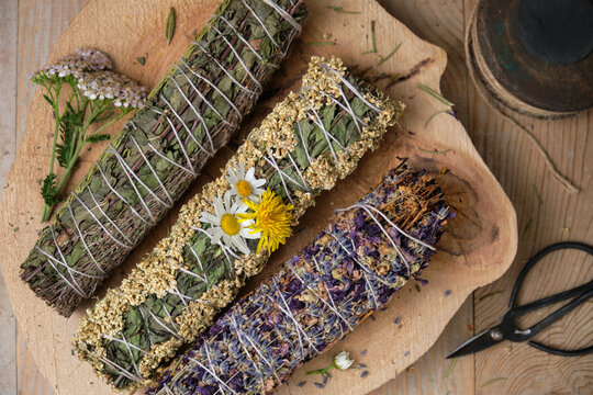 Three hand-bound herbal incense bundles with dried herbs on wooden table
