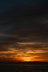 Fototapeta premium 夏の瀬戸内海で日没後に厚い雲の下へ橙色が残る夕焼けの空と山並み