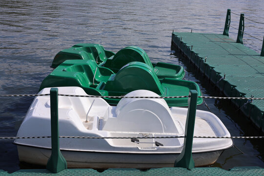 Row of green and white pedal boats moored at floating dock on lake
