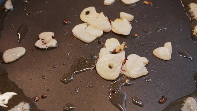 Saut&eacute;ing sliced ​​garlic cloves in olive oil in a frying pan, close-up view.