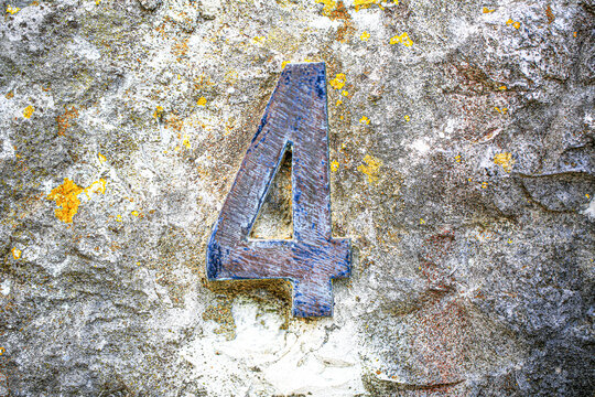 House number four sign in aged metal, mounted on a rugged rock wall, displaying a single weathered numeral with rustic tarnished metallic surface finish