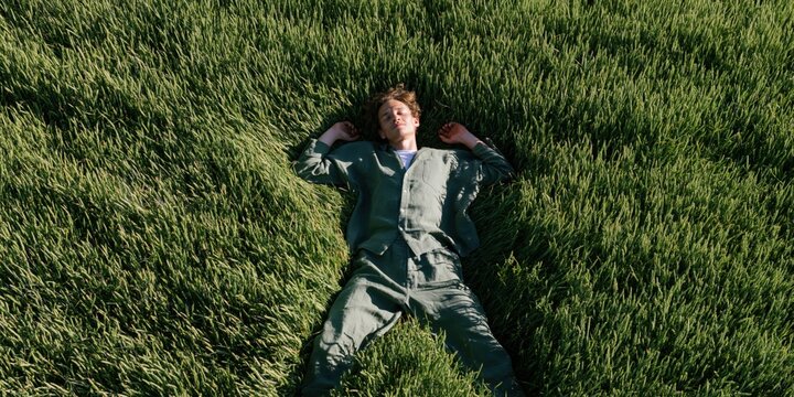 Aerial view of a man in a green outfit lying in tall grass for wellness background and nature poster design