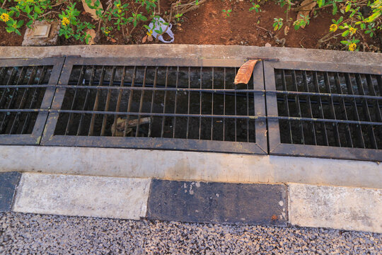 Black Iron Drainage Grate Trench Cover on Concrete Curb Street Gutter in Public Park