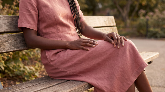 Woman sitting on park bench in pink dress, hands resting on lap, finding moments of solitude outdoors