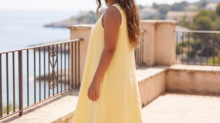 Naklejka premium Woman enjoying coastal resort balcony view on vacation, wearing a breezy yellow summer dress