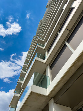 Tall building under blue sky. A modern building stands tall with several balconies. The bright blue sky has some clouds around it.