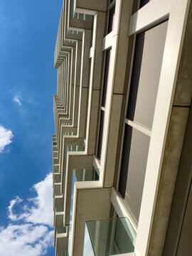 Building design with blue sky view. The image shows a modern building with a blue sky and clouds above. The structure has many floors and balconies.