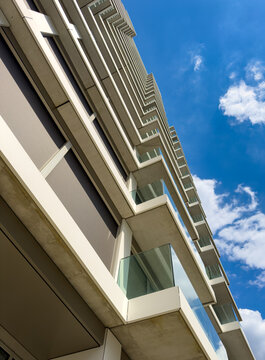 View of a tall building under a blue sky. A tall building with balconies stands under a bright blue sky. Fluffy white clouds are visible above the structure.
