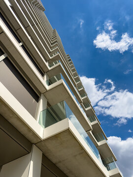Contemporary high rise building with glass balconies. An upward perspective of a tall modern architectural structure featuring concrete balconies under a bright blue sky.