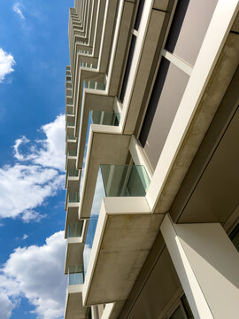 Vertical view of modern building facade and balconies. A bottom up perspective displays concrete balconies and glass railings of a tall building beneath a cloudy sky.
