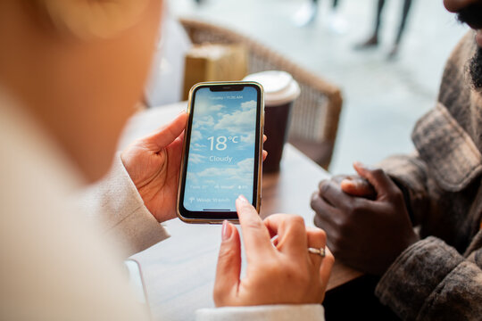 Friends checking weather app on smartphone at cafe table