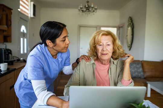 Caregiver helping senior woman use laptop at home