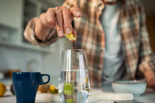 Person squeezing lemon into glass of water in home kitchen