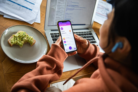 Person using mobile banking app at home office with laptop and avocado toast