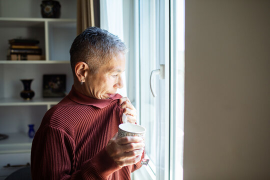 Mature person drinking tea by window at home