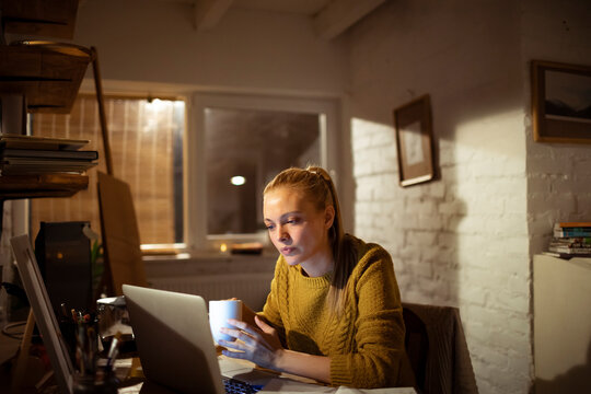 Young woman working late at home office with laptop and coffee