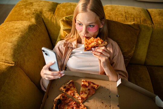 Young woman relaxing on couch with pizza and smartphone at home