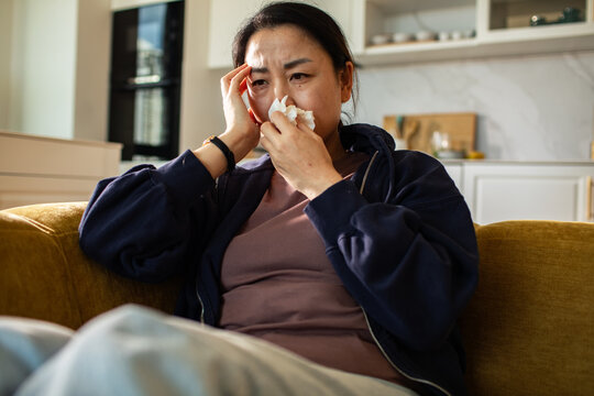 Concerned woman on sofa at home using tissue