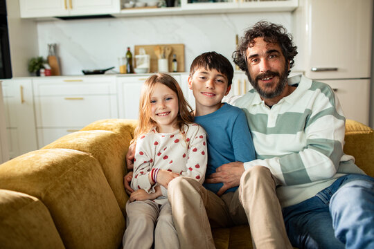 Smiling father with son and daughter on sofa at home