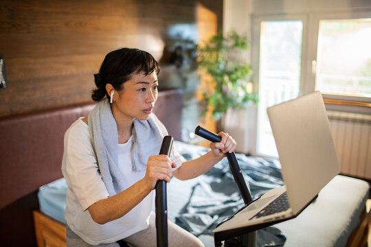 Woman cycling on a stationary bike at home with laptop