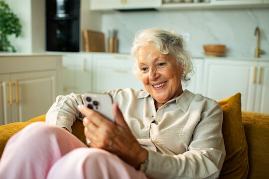 Smiling senior woman using smartphone on sofa in modern kitchen